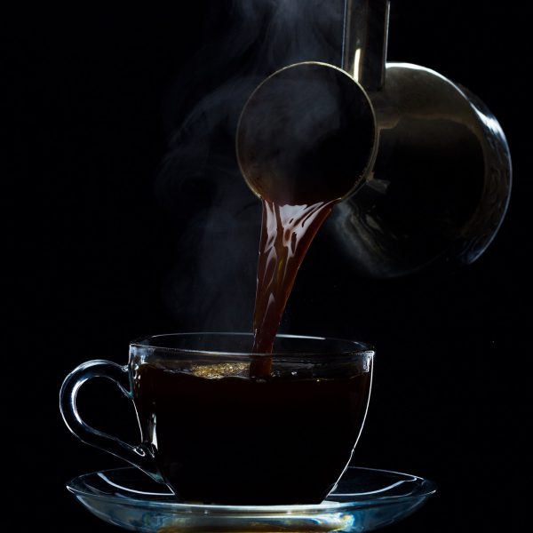 Coffee is poured into a glass cup from the Turks, a black background
